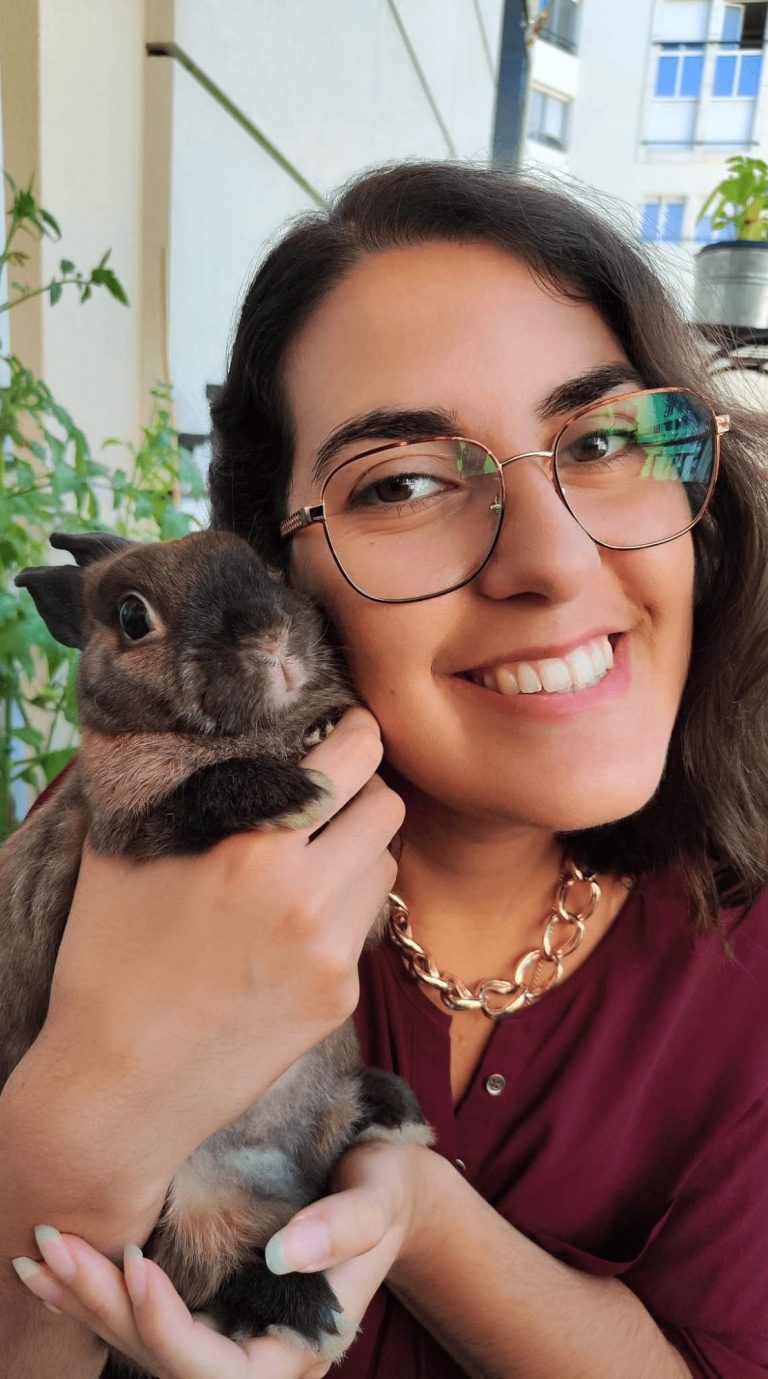 Femme souriante tenant un lapin dans ses bras, entourée de plantes.